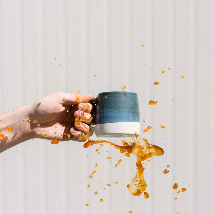 Coffee spilling out of mug against white wall